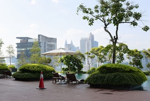 A rooftop pool area with lounge chairs and a large umbrella, surrounded by greenery and overlooking a city skyline. - Nusareka Homestay (Kuala Lumpur)