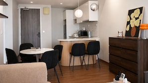 Un espacio habitable compacto con kitchenette, una zona de comedor con mesa y sillas redondas, y un pequeño rincón de estar con sofá.