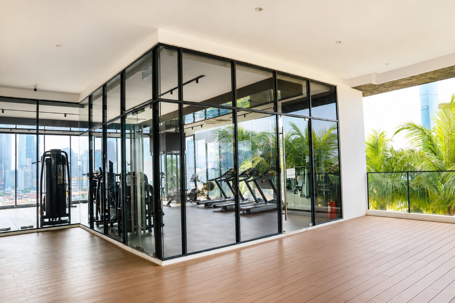 A modern gym with exercise equipment, large windows, and a view of palm trees and a cityscape.