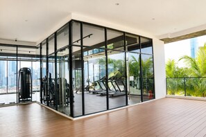 Un gimnasio moderno con equipamiento de ejercicio, amplias ventanas y vistas a palmeras y al horizonte de la ciudad.