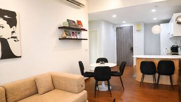 A modern living room with a sofa, a dining table with chairs, a kitchen area with a counter and chairs, and a hallway leading to a door.