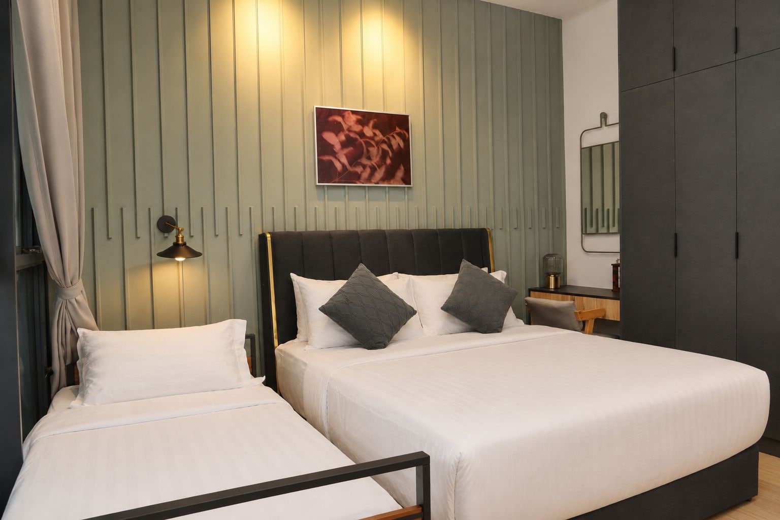 A double bed with a black headboard and two pillows, a bedside table with a lamp, and a green wall with vertical lines.