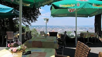 Ein Außenbereich mit Tischen und Stühlen, grünen Sonnenschirmen und Blick auf eine Stadtlandschaft.