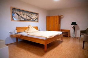 Quarto com cama de madeira, mesa de cabeceira, abajur, guarda-roupa e uma cadeira.