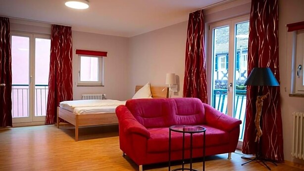 Et værelse med en seng, en rød sofa, et lille bord og en lampe.
