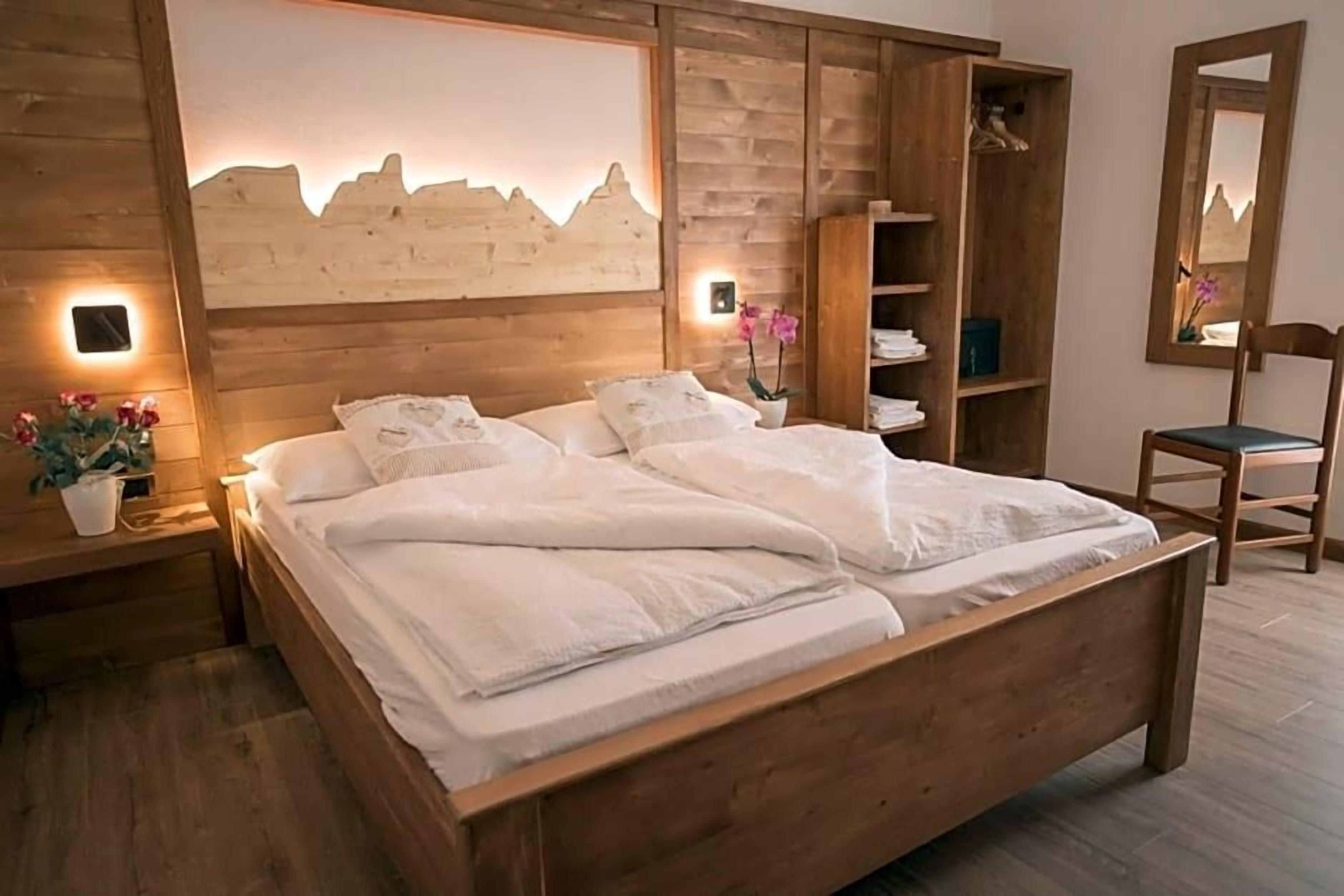 Un lit en bois avec une literie blanche, une table de chevet ornée d’un vase de fleurs et une armoire en bois avec des étagères.