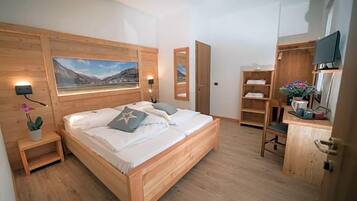 Un lit en bois avec vue sur la montagne, une petite table de chevet agrémentée d’une plante, et un bureau en bois avec une chaise.