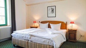 A hotel room with a double bed, two bedside tables with lamps, a framed picture on the wall, and a radiator. - Brauhaus In Spandau (Berlin)