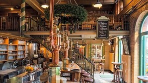A bar area with a staircase, bar stools, and a hanging plant. - Brauhaus In Spandau (Berlin)
