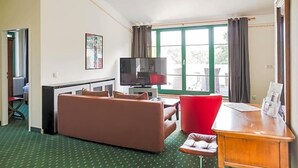 A living room with a sofa, a red chair, a wooden desk, and a television. - Brauhaus In Spandau (Berlin)