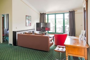 Ein Wohnzimmer mit einer Couch, einem roten Sessel, einem Holztisch und einem Fernseher.