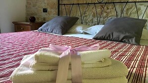 A neatly made bed with a striped bedspread, a stack of folded towels with a ribbon, and a stone wall in the background. - Masseria Monte Pizzi (Carovilli)