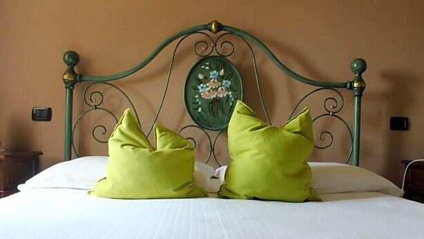 A bed with a metal headboard, two pillows, and a wall-mounted decorative plate. - Masseria Monte Pizzi (Carovilli)