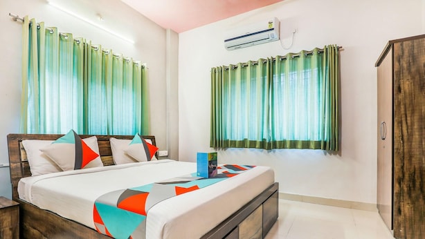 Una habitación de hotel con una cama de madera, dos ventanas con cortinas, un armario y un equipo de aire acondicionado.
