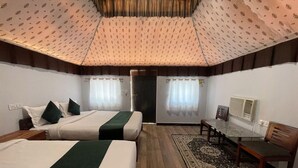 A hotel room with two beds, a small table, a chair, a radiator, and a door. - Unity Holiday Resort (Garudeshwar)