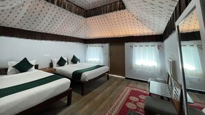A hotel room with two beds, a red patterned rug, a television, and a ceiling with a patterned design. - Unity Holiday Resort (Garudeshwar)