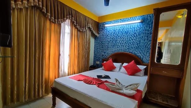 Een hotelkamer met een bed, gordijnen, een spiegel en een muur met een blauw patroon.