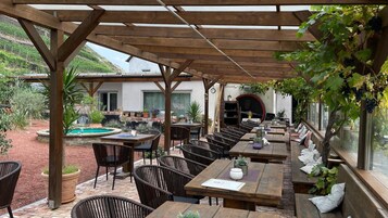 Un patio exterior con mesas y sillas de madera, una piscina y vistas a una colina.