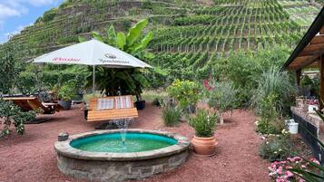 Ein Garten mit einem Brunnen, einer Bank und einem Tisch mit Sonnensegel.