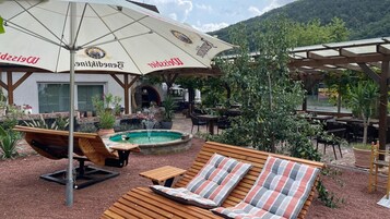 Un área de estar al aire libre con tumbonas de madera, piscina y sombrillas.