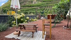 Un jardin avec une table et un banc de pique-nique en bois, entouré de différentes plantes et d’un petit arbre.