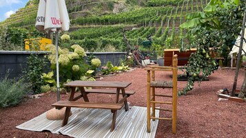 Un jardín con una mesa de picnic y un banco de madera, rodeado de diversas plantas y un árbol pequeño.