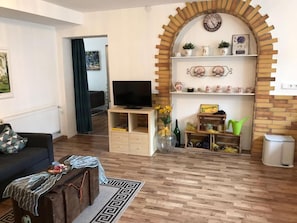 Un salon comprenant un téléviseur, un canapé, une table basse, une bibliothèque et un arc décoratif en briques.
