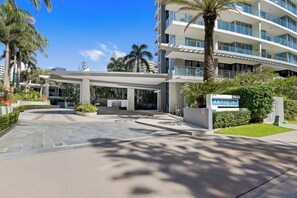 A modern hotel entrance with a covered walkway, palm trees, and a sign for the Artique hotel. - The Enderley 2 Bedroom (Surfers Paradise)