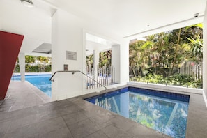 Una piscina con borde de azulejos, barandilla metálica y un cartel con las normas del spa.
