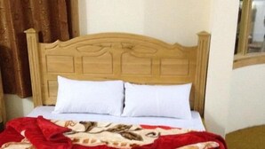 Cama com cabeceira de madeira, almofadas brancas e manta florida vermelha.
