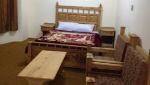 Quarto com cama de madeira, mesa de cabeceira, uma cadeira e uma mesinha.