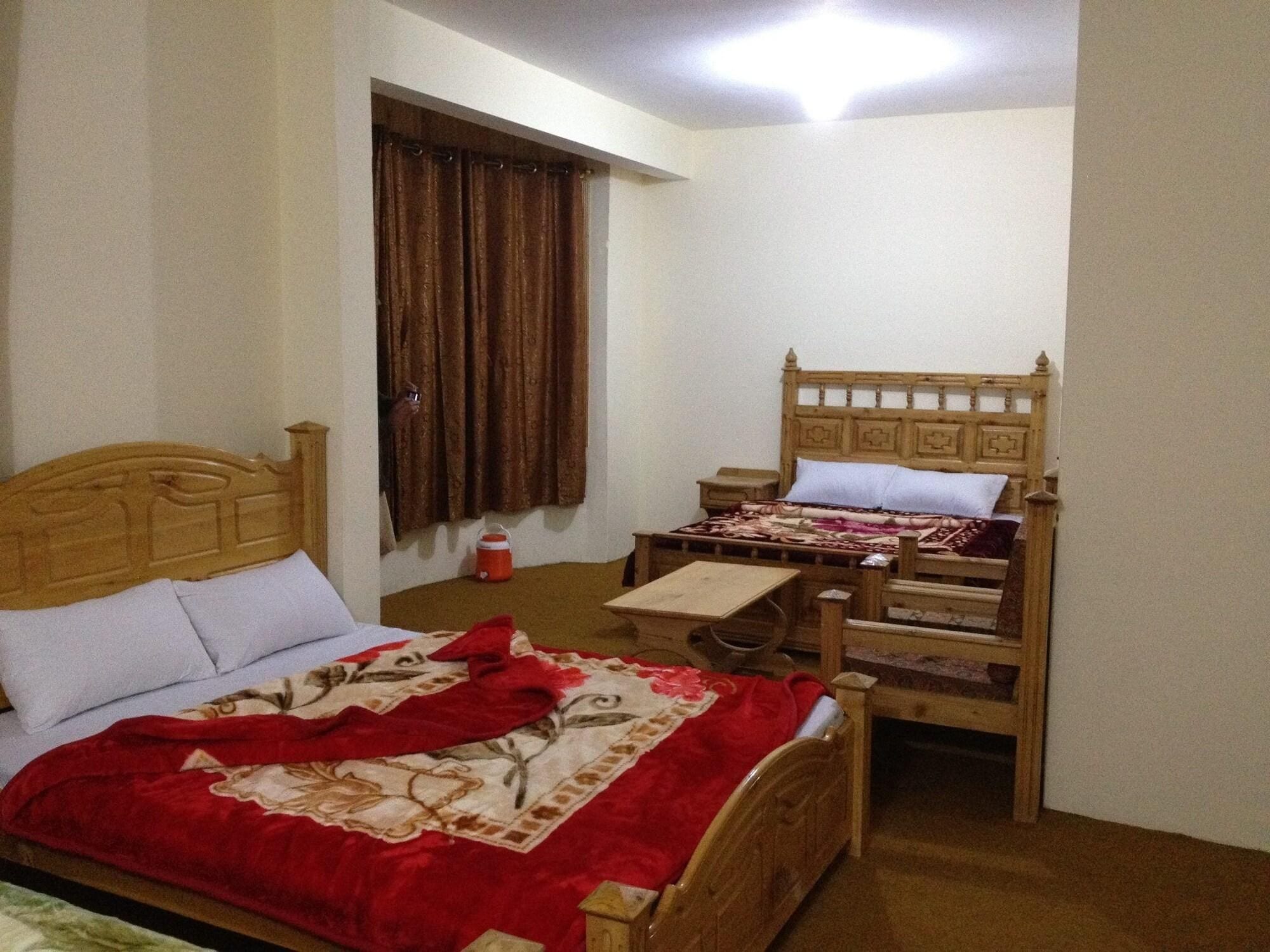 A bedroom with two wooden beds, a nightstand, a small table, and a window with curtains.