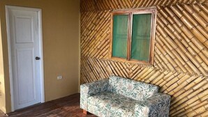 Una habitación con suelo de madera, una puerta blanca, un sofá con estampado de hojas y una pared de bambú.