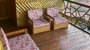 Una terraza de madera con dos sillas y un banco, un muro de bambú y vistas al verdor.