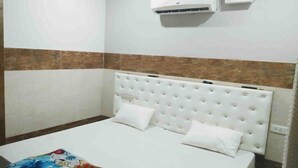 Una habitación con cama, paredes blancas, parte inferior marrón, aire acondicionado y un reloj.