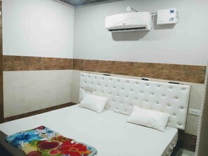 Una habitación con cama, paredes blancas, parte inferior marrón, aire acondicionado y un reloj.