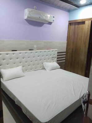 Una cama con cabecera, una puerta de madera y un equipo de aire acondicionado en la pared.