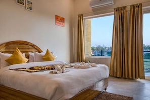 A hotel room with a large bed, a wooden headboard, and a view of the city through the window. - Pristine Nature View By Group Of Hotels18 (Ramnagar)