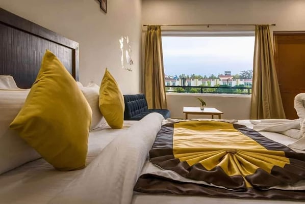 A hotel room with two beds, a small table, and a view of the city. - Pristine Nature View By Group Of Hotels18 (Ramnagar)