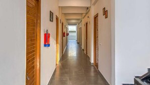 A long, narrow hallway with wooden doors on both sides, a fire extinguisher mounted on the wall, and a fire hose visible in the distance.