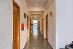 A long, narrow hallway with wooden doors on both sides, a fire extinguisher mounted on the wall, and a fire hose visible in the distance. - Pristine Nature View By Group Of Hotels18 (Ramnagar)