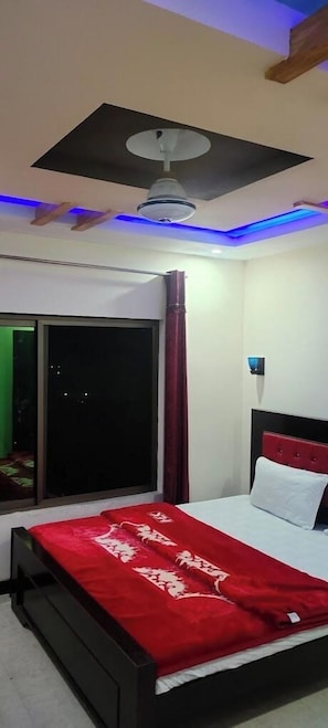 A bedroom with a bed, a ceiling fan, a window with curtains, and a red accent wall. - Hotel Valley Door (Balakot)