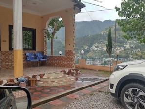 A covered outdoor seating area with chairs, a tiled floor, and a view of a hilly landscape. - Hotel Valley Door (Balakot)