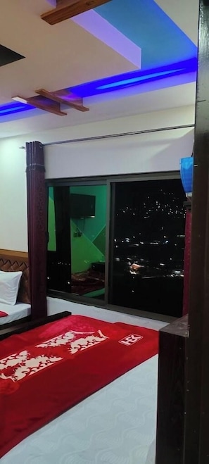 A bedroom with a bed, a red runner, a window with a night view, and a ceiling with blue lighting. - Hotel Valley Door (Balakot)