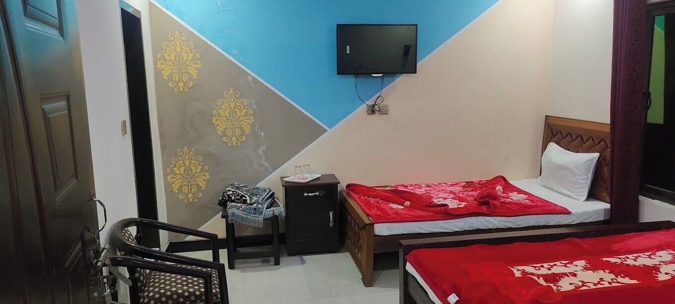 Un dormitorio con una cama, televisor montado en la pared, una silla y una mesita.