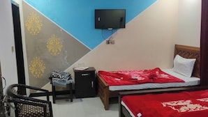 Un dormitorio con una cama, televisor montado en la pared, una silla y una mesita.