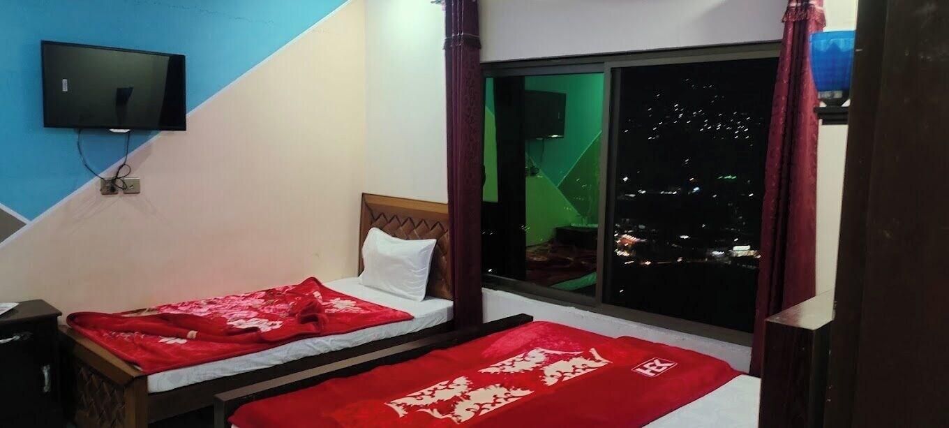 Una habitación con dos camas, un televisor montado en la pared y una ventana con vista a la ciudad de noche.