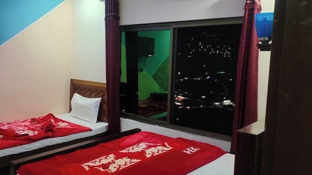 Una habitación con dos camas, un televisor montado en la pared y una ventana con vista a la ciudad de noche.