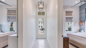 A hallway leading to a bedroom with a herringbone floor, a bed, and a bedside table. - Boardwalk Breeze 109 Sou (Port Aransas)