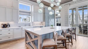 A modern kitchen with a large island, grey cabinets, and hanging spherical light fixtures. - Boardwalk Breeze 109 Sou (Port Aransas)